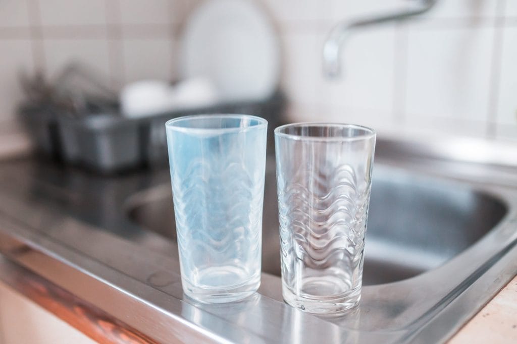 Stock image showing a dirty glass washed in hard water and a clean glass cleaned with water softener treated water.