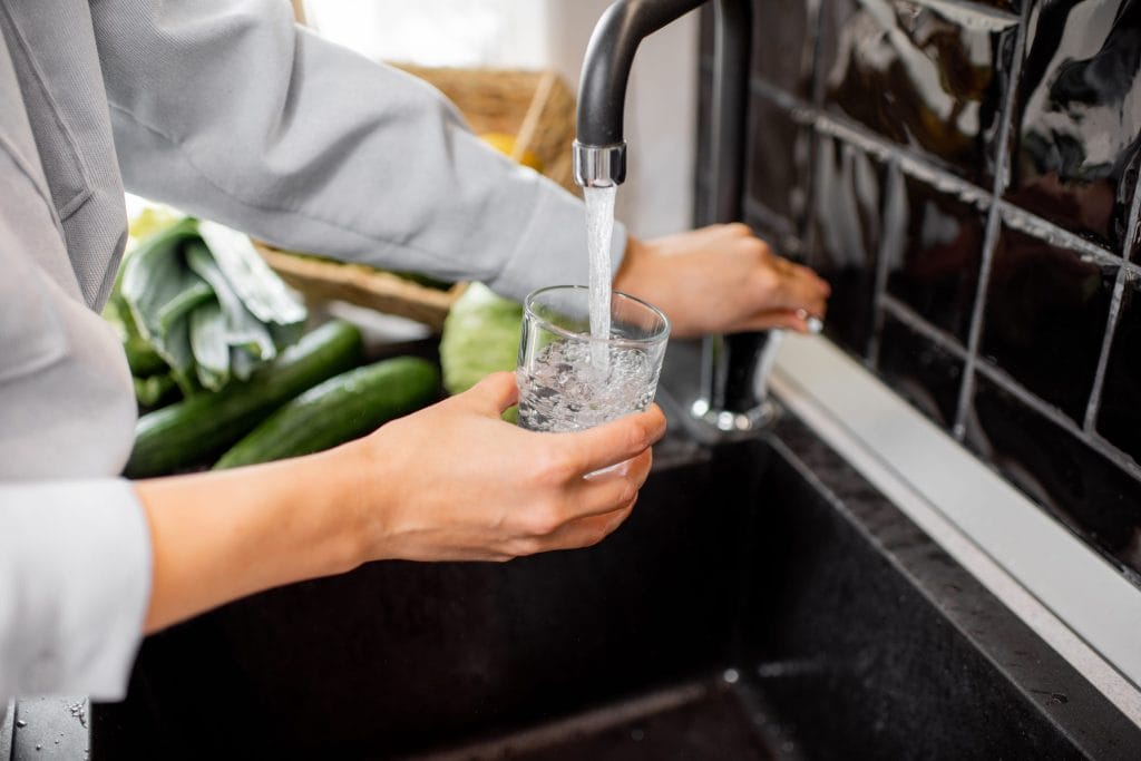 A stock image of a resident filling up a glass of water from their sink.