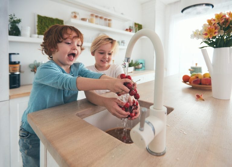 Stock image of two kids washing their hands in a sink with tap water.