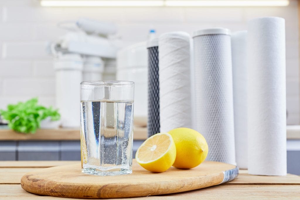 Stock image of a glass of filtered clean water with reverse osmosis filters in the background.