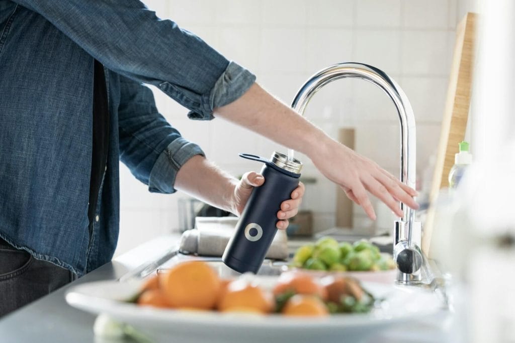 Stock image of a person filling a water bottle from their kitchen sink.