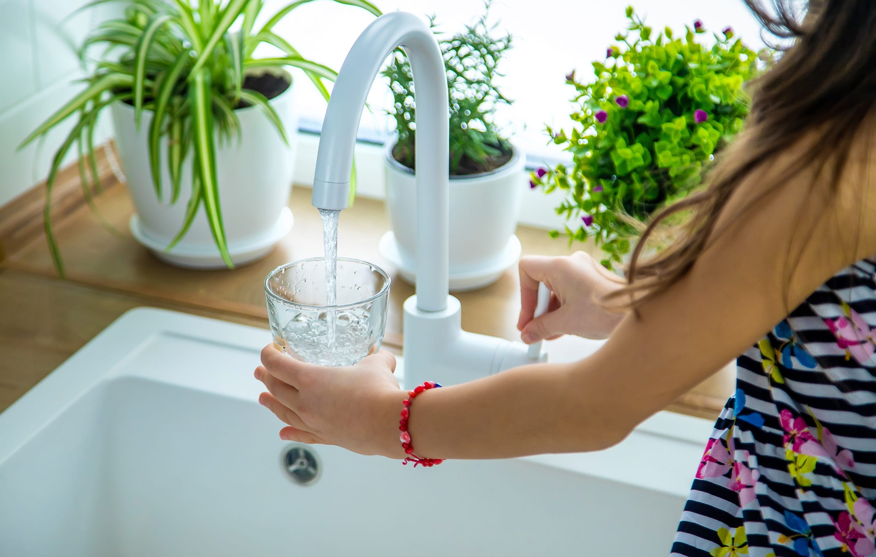 Stock image of girl pouring herself a glass of water from the faucet.